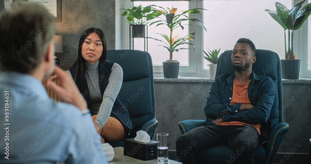 Back view of unfocused psychologist talking to young family during couples therapy. African American young man discusses relationship problems. Multiethnic couple on counseling session with therapist. Back view of unfocused psychologist talking to young family during couples therapy. African American young man discusses relationship problems. Multiethnic couple on counseling session with therapist.