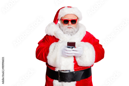 Portrait of minded santa claus with eyewear eyeglasses using cell phone device reading news wearing costume isolated over red background