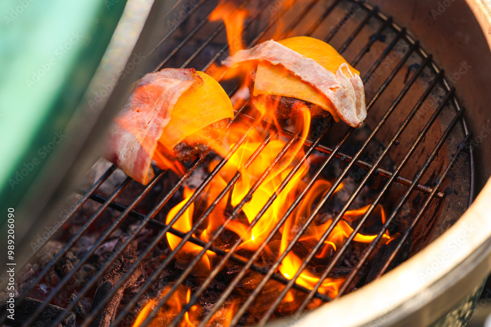 Barbecue party. Close up photo with some burger meat, cheddar and bacon on a charcoal ceramic grill. Grilled meat for outdoor eating.