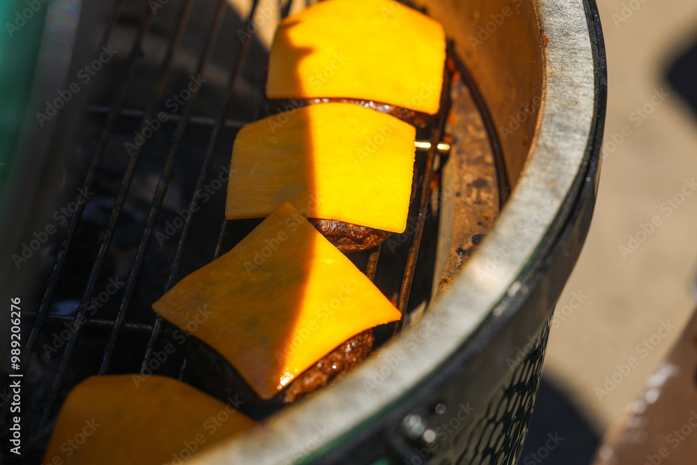 Barbecue party. Close up photo with some burger meat, cheddar and bacon on a charcoal ceramic grill. Grilled meat for outdoor eating.
