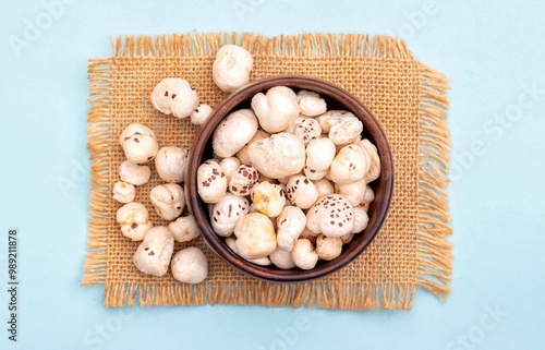Top View of Makhana or Fox Nut in a Wooden Bowl on Burlap Fabric Isolated on Light Blue Background with Copy Space, Also Known as Lotus Seed Pop, Euryale Ferox or Gorgon Nut