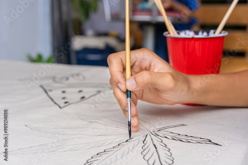 Close-up hand holding paintbrush while painting abstract on canvas for art, craft, with a red cup. Hobby and leisure concept. Relaxing art at home.