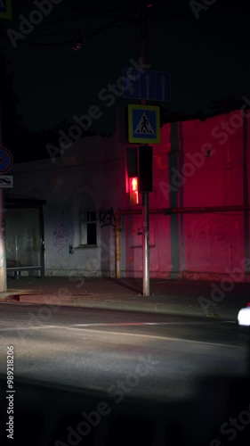 Cinematic night street. The urban color. Bright led traffic light. The old wall. Pedestrian crossing. Bus stop. The road is almost empty. A car interchange. It's late at night. A tableau with numbers.