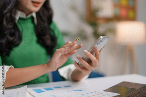 Businesswoman is using a smartphone and stylus pen while reviewing financial charts and graphs at her desk photo