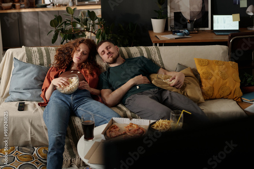 Canvas Print Young relaxed couple with popcorn napping on comfortable couch in front of table