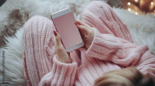 Top view of woman relaxing on sofa and scrolling through phone screen while she is shopping online. Bright lighting, elegant colors and soft pink. Simple items in the image.
