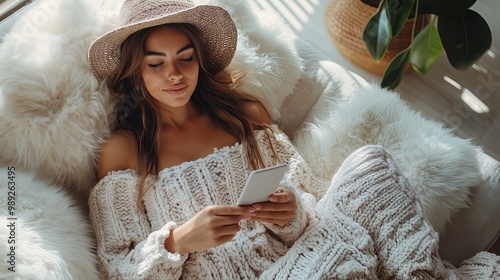 Top view of woman relaxing on sofa and scrolling through phone screen while she is shopping online. Bright lighting, elegant colors and soft pink. Simple items in the image.

