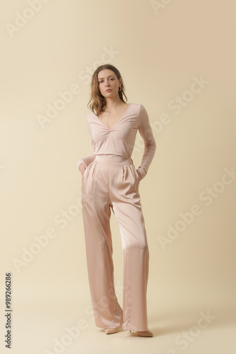 Female model wearing monochrome pale pink outfit. Classic and timeless simple blouse and wide legs trousers. Fashion studio shot.