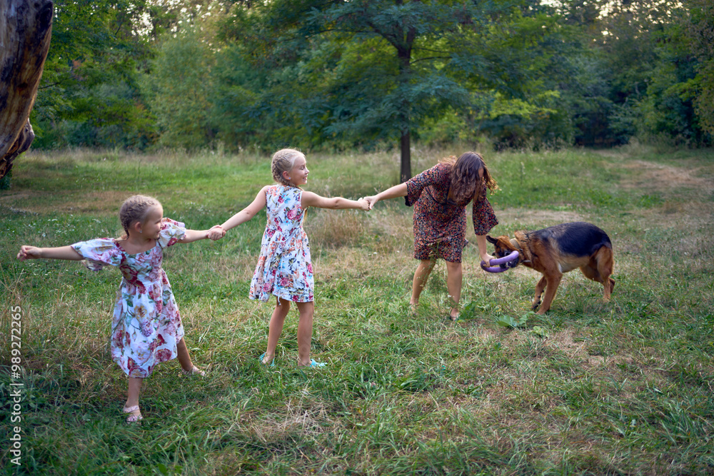 Obraz premium mom and little girls sisters playing with german shepherd dog during easter picnic in the garden