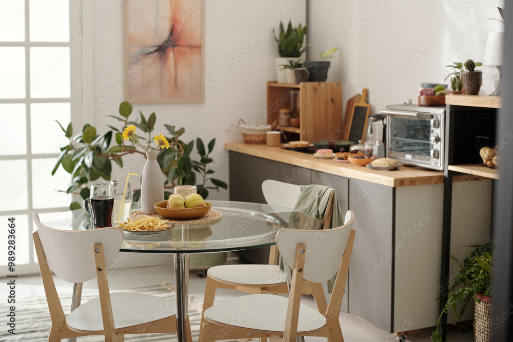 Three chairs surrounding glass kitchen table with vase, two drinks with straws, french fries on plate and bowl with ripe apples Three chairs surrounding glass kitchen table with vase, two drinks with straws, french fries on plate and bowl with ripe apples