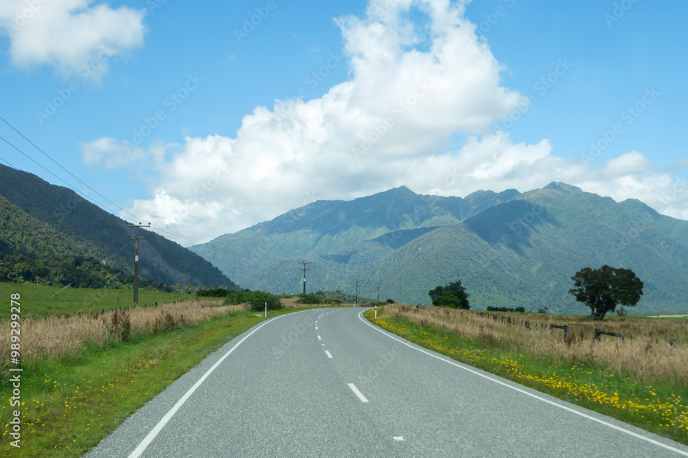 Naklejka premium A journey roadtrip to the countryside full of fresh green meadow farmland and range of mountains landscape view in the summer, West Coast, South Island, New Zealand.