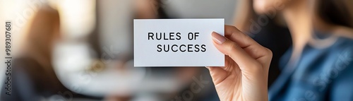 Close-up of a person's hand holding a card that reads 'Rules of Success' in an office setting, emphasizing business principles.