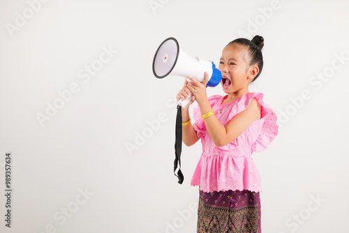 Portrait Thailand kid girl smiling traditional Thai dress costume shouting by megaphone, studio shot isolated white background, kindergarten screeching through in megaphone announces discounts