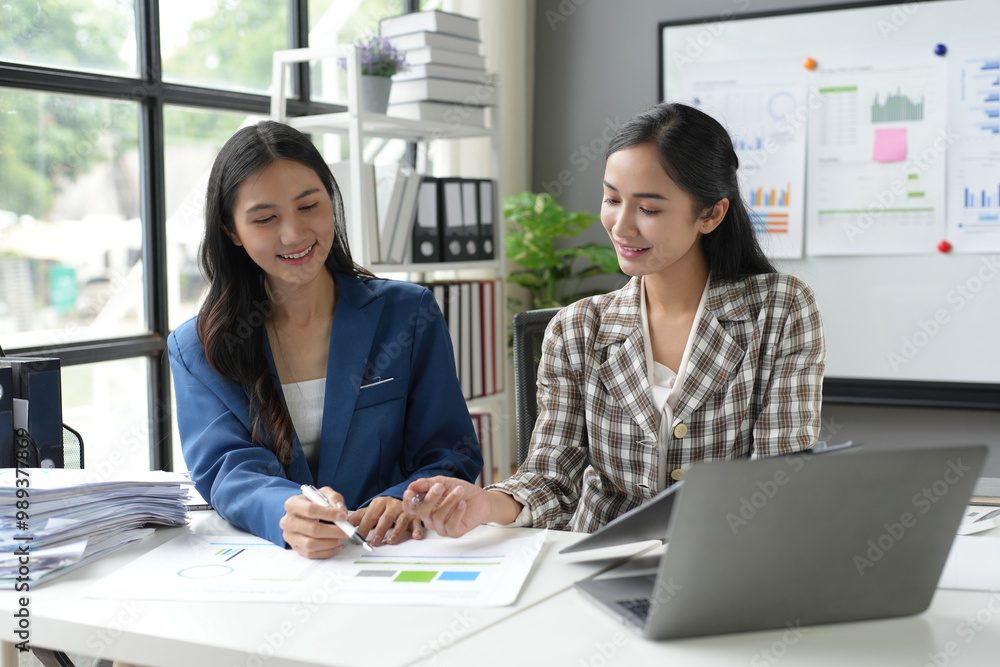Obraz premium Two asian businesswomen are having a discussion over financial charts and reports using laptop at the office