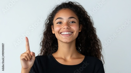 A young woman with a big smile is pointing upwards with her finger. She's standing against a plain white background.