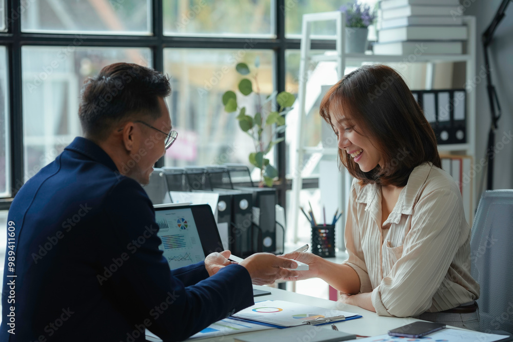 Two business partners smiling and discussing a project together, analyzing financial charts and using a digital tablet Two business partners smiling and discussing a project together, analyzing financial charts and using a digital tablet