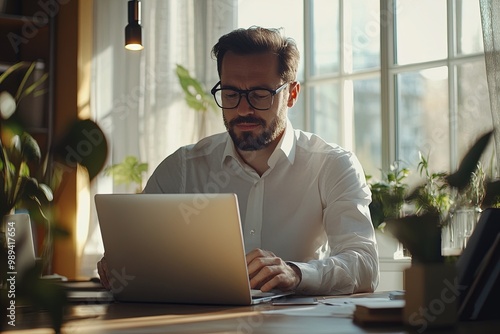 A Man Working on a Laptop Surrounded by Plants in a Sunlit Home Office, Enjoying a Productive Moment in the Afternoon