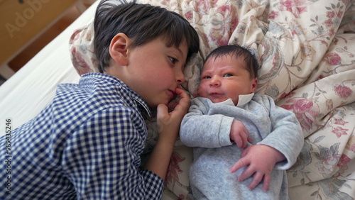 Older brother lying side by side with newborn sibling on a bed, sharing a close and heartwarming moment of bonding that emphasizes the love and affection between the two siblings