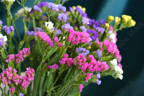 Bouquet of multicolored flowers in a vase (Limonium sinuatum, Statice sinuata) on a green background photo