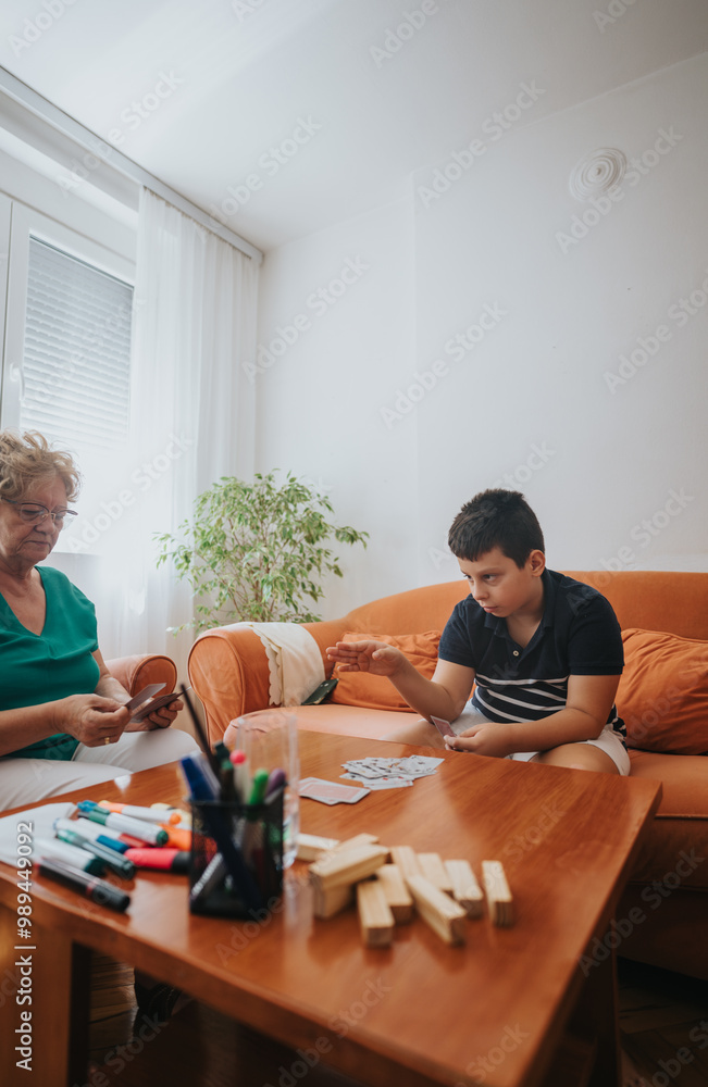 Obraz premium A grandmother and her grandson play a card game in a warm living room, surrounded by family-friendly decor, encouraging love and bonding through playful interaction.