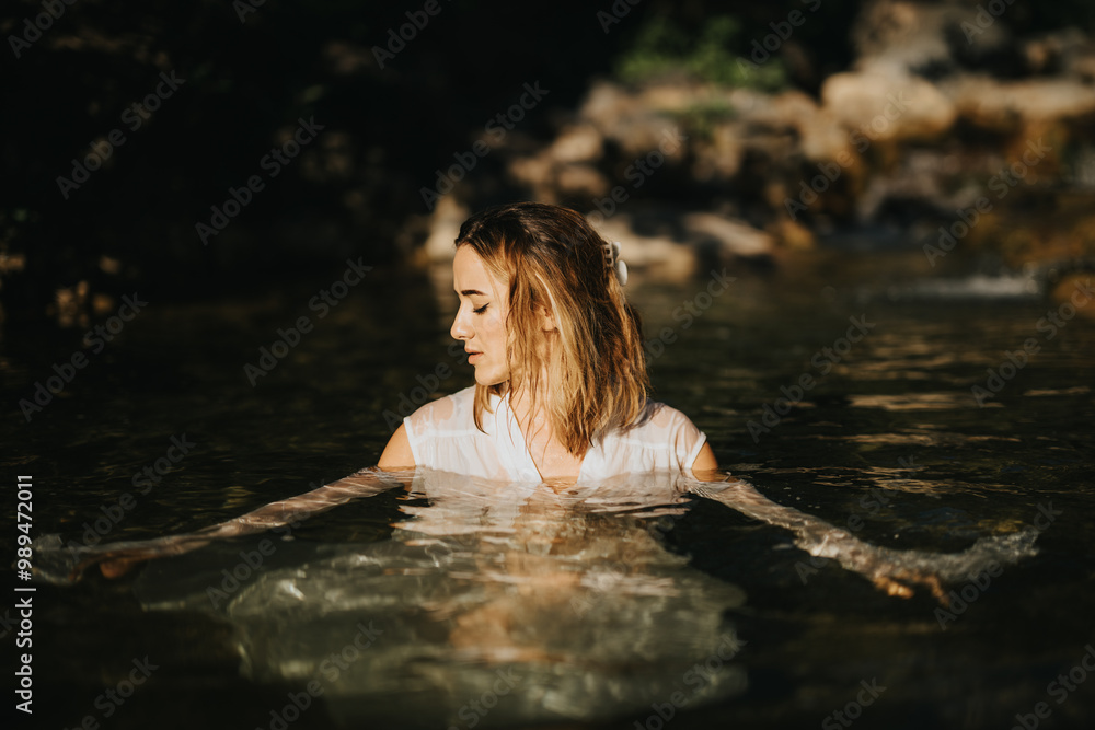 Fototapeta premium A woman immersed in clear water with a nature background, exuding a serene and contemplative mood. Perfect for themes of tranquility, relaxation, and natural beauty.