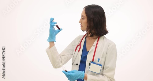 Young woman doctor observes blood specimen carefully on white background. Professional physician holds test tubes containing blood samples