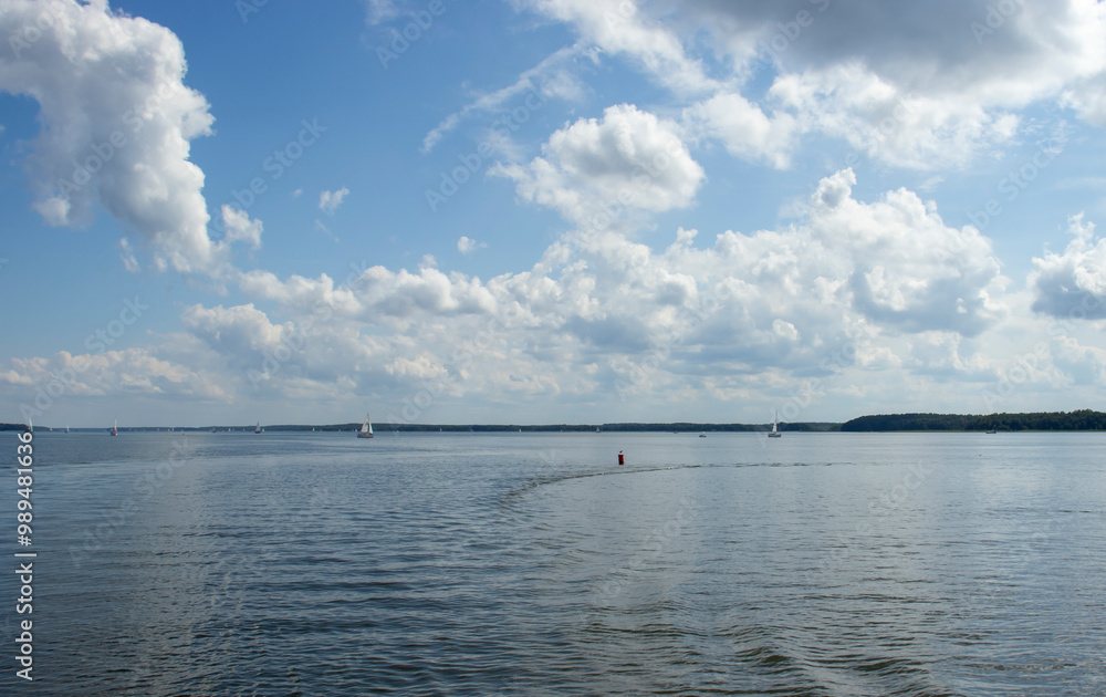 A serene lake scene with sailboats gliding on calm waters and fluffy clouds scattered in a bright blue sky. Ideal for nature and outdoor themes. A serene lake scene with sailboats gliding on calm waters and fluffy clouds scattered in a bright blue sky. Ideal for nature and outdoor themes.