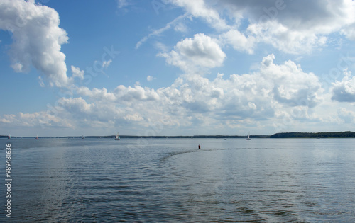 A serene lake scene with sailboats gliding on calm waters and fluffy clouds scattered in a bright blue sky. Ideal for nature and outdoor themes. photo