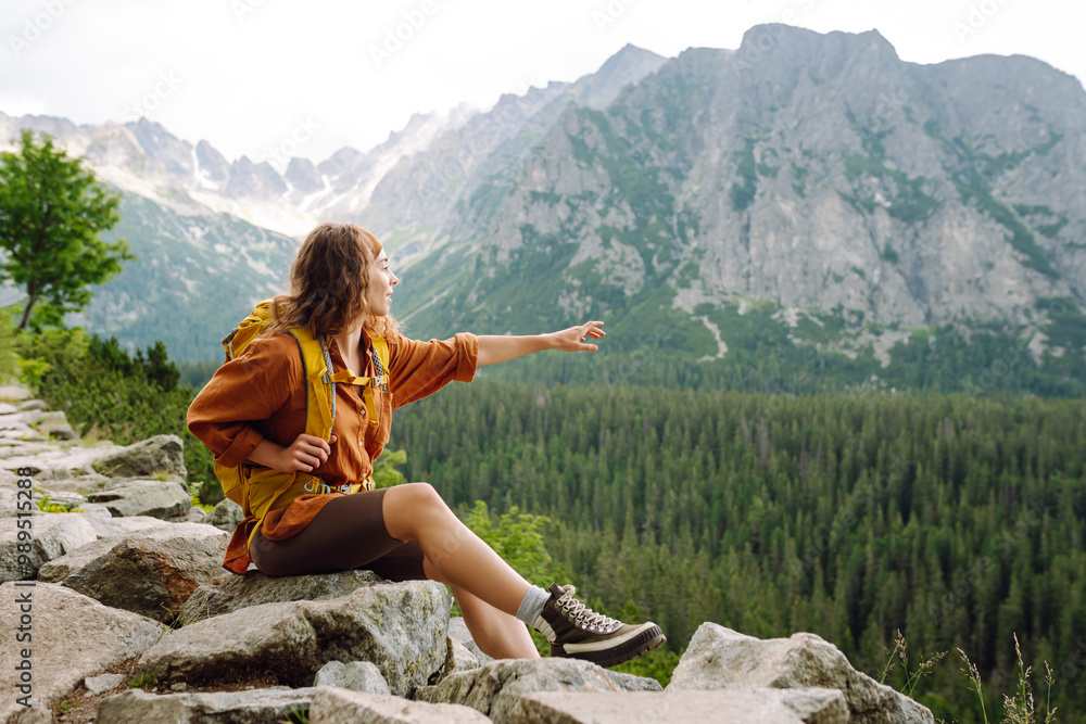 Naklejka premium A hiker enjoys the fresh mountain air while trekking a rocky trail through the lush green landscape in the afternoon light. Concept of an active lifestyle.