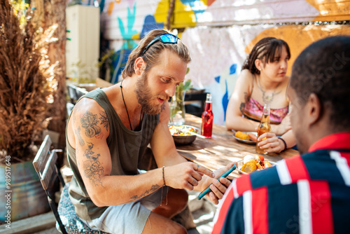 Wallpaper Mural Friends gathered at an outdoor hostel area while one shows something on a smartphone Torontodigital.ca