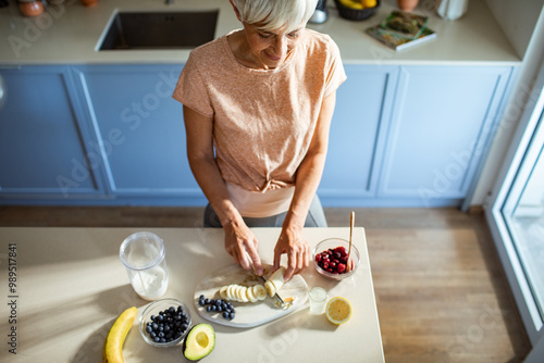 Senior woman preparing a healthy smoothie with fresh fruits in a modern kitchen