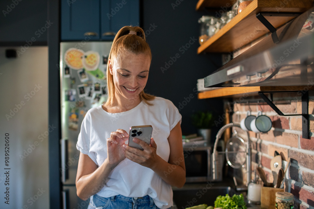 Smiling young woman using smartphone in modern kitchen
