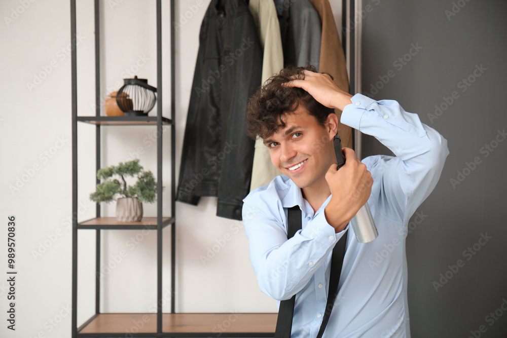 Handsome young man applying hair spray on his curly hair in hallway Handsome young man applying hair spray on his curly hair in hallway