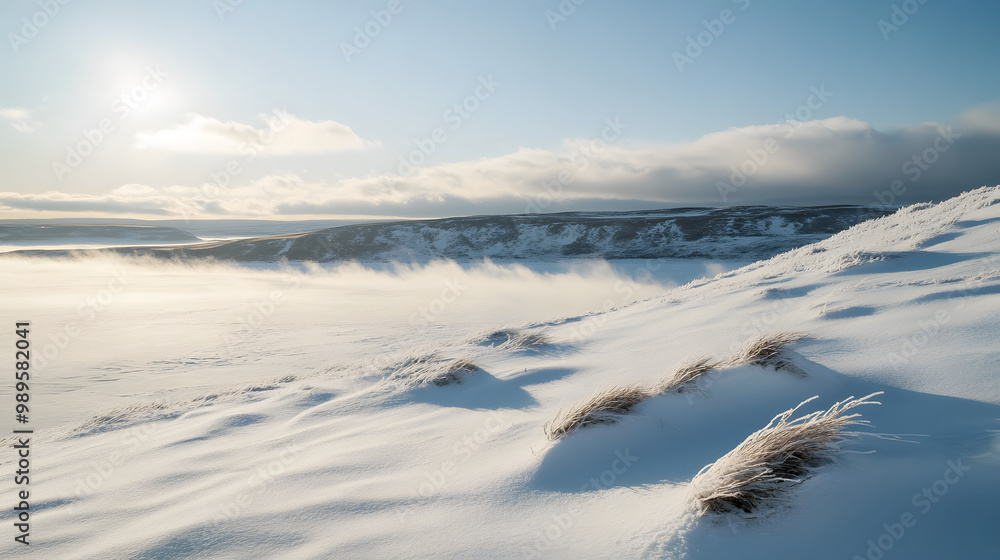 A snowy hilltop overlooking a frozen lake with low clouds hanging over the horizon and the wind sweeping across the snow creating ripples and patterns.