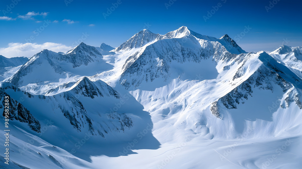 A vast snow-covered mountain range under a deep blue sky with the bright sunlight casting sharp shadows across the slopes.