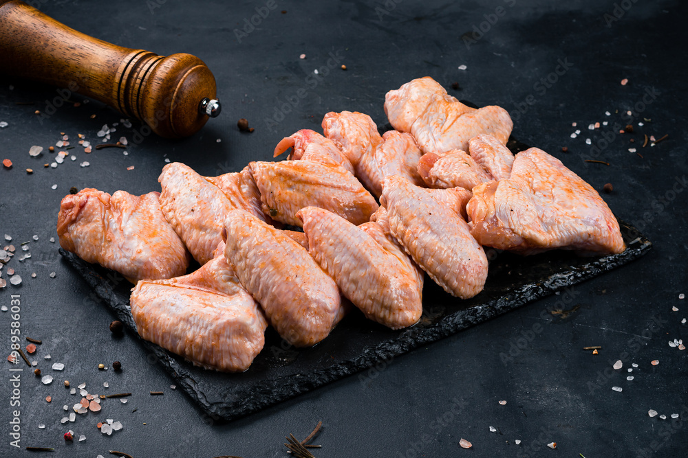 Raw marinated barbecue chicken wings in sauce and spices on a dark background.