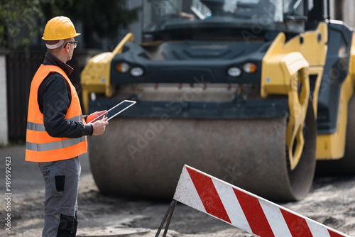 Bilde på lerret Construction worker inspecting roadwork with a tablet near a steamroller at a bu