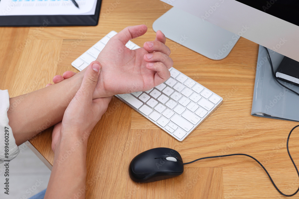 Man suffering from pain in wrist while working on computer at wooden table, closeup. Carpal tunnel syndrome Man suffering from pain in wrist while working on computer at wooden table, closeup. Carpal tunnel syndrome