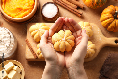 Woman making pumpkin shaped buns at brown table, top view photo