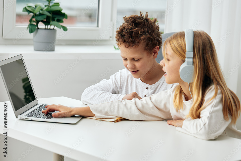 Happy children learning online with laptops and headphones at home A brother and sister sitting at a table in the living room, focused and concentrated on their educational activities They are Happy children learning online with laptops and headphones at home A brother and sister sitting at a table in the living room, focused and concentrated on their educational activities They are
