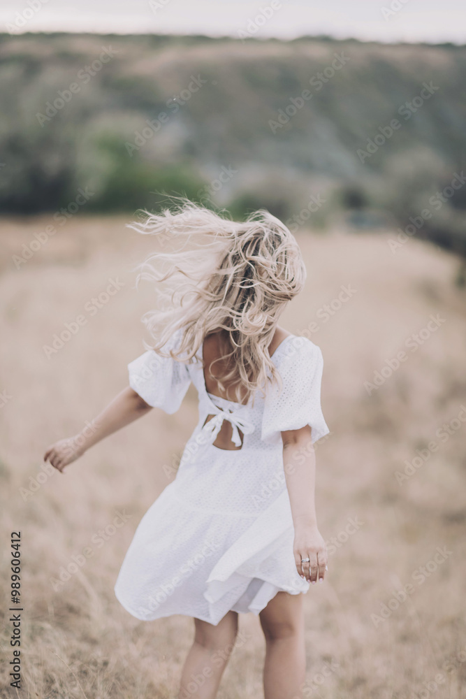 A girl with blond curly hair and in a romantic dress stands in the middle of the field. The wind develops the girl's hair. Lonely girl in nature. Concept of freedom, happiness, dreaming, purity, relax A girl with blond curly hair and in a romantic dress stands in the middle of the field. The wind develops the girl's hair. Lonely girl in nature. Concept of freedom, happiness, dreaming, purity, relax