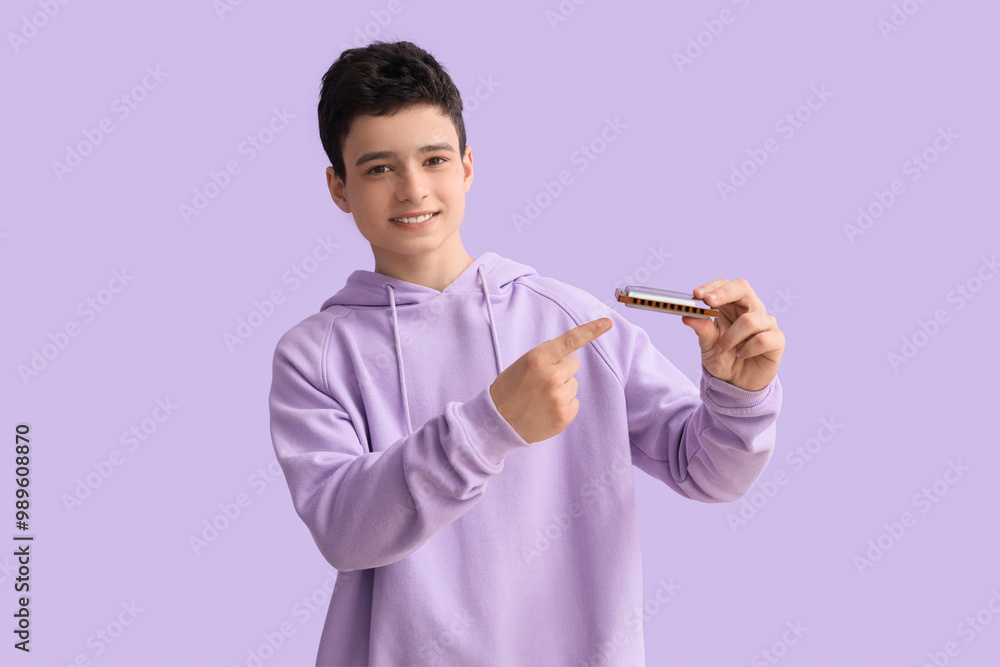 Teenage boy pointing at harmonica on lilac background Teenage boy pointing at harmonica on lilac background
