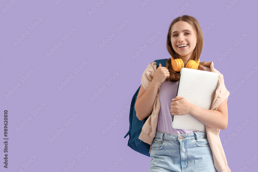 Happy female student with backpack, headphones and laptop on purple background Happy female student with backpack, headphones and laptop on purple background