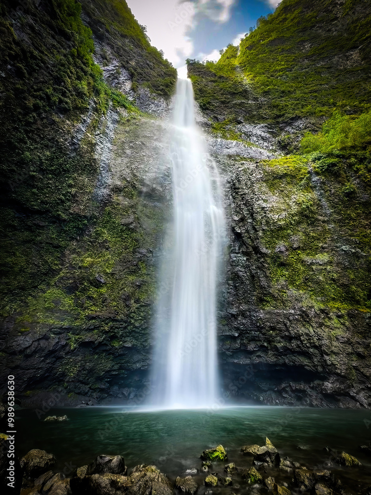Fototapeta premium Long exposure scenic view of Hanakapiai Falls, a waterfall at the end of Hanakapiai Valley hiking trail, Kauai, Hawaii, USA against blue sky with clouds