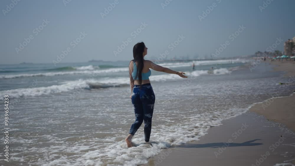 Young girl Caucasian woman with long brunette hair walking with her back to the camera on the sand of the beach blows a kiss to the camera Young girl Caucasian woman with long brunette hair walking with her back to the camera on the sand of the beach blows a kiss to the camera
