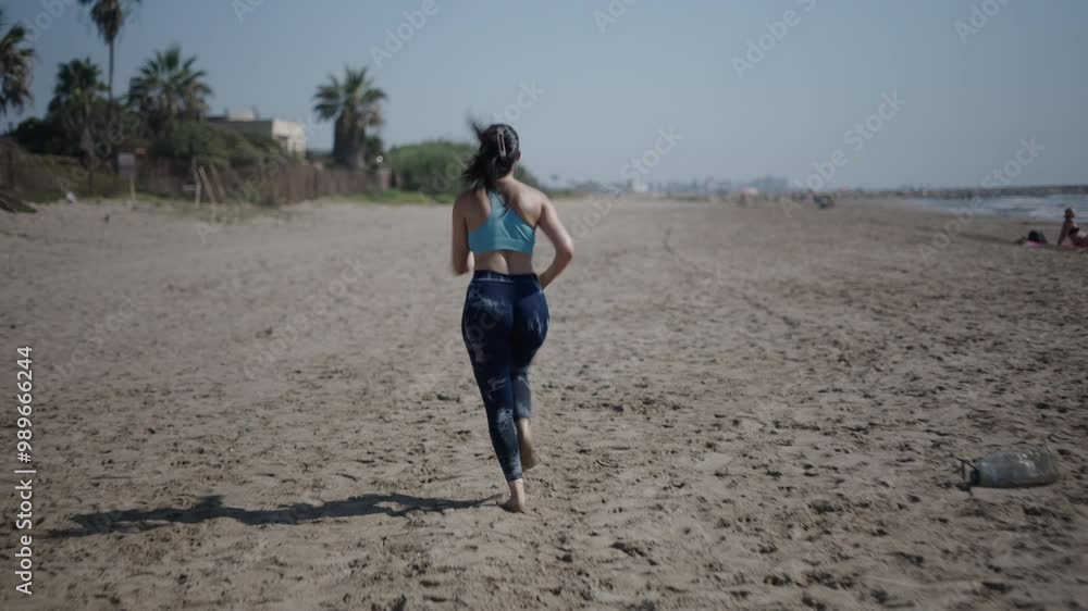 Young brunette Caucasian woman girl with long hair running and doing sports with her back to camera on the beach sand barefoot Young brunette Caucasian woman girl with long hair running and doing sports with her back to camera on the beach sand barefoot