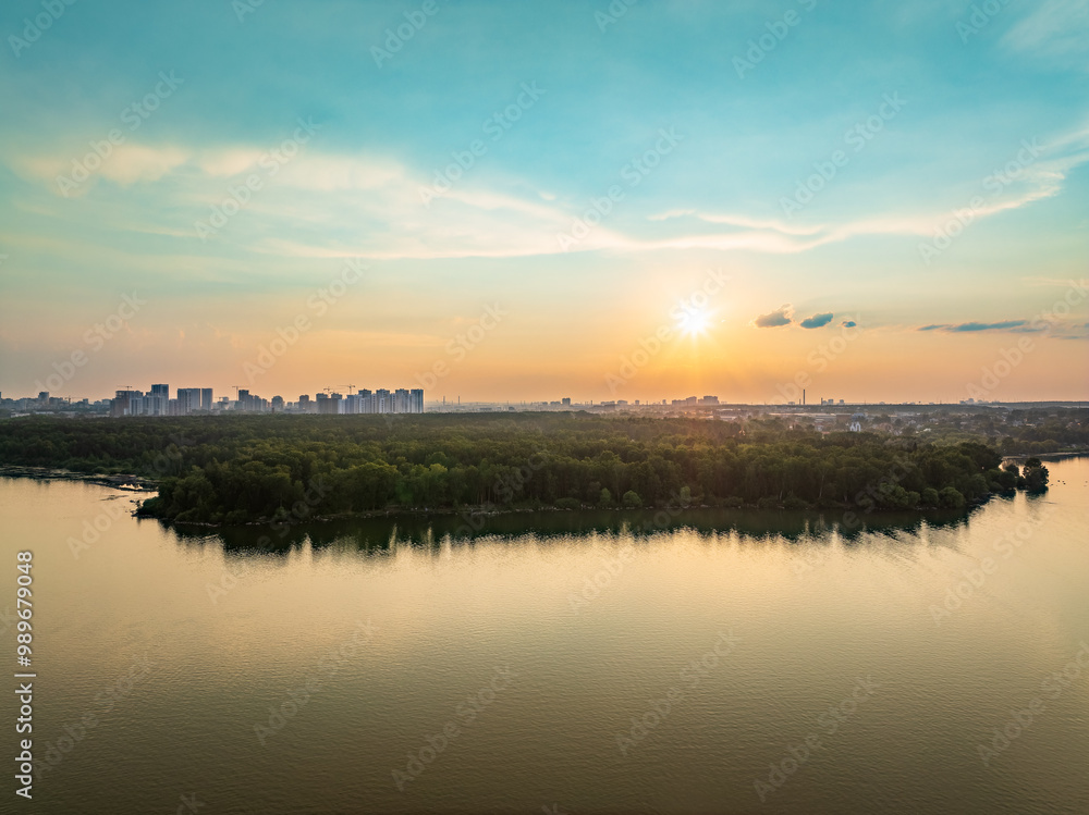 Obraz premium Big lake with green shores in bright sun light and city on horizon, aerial landscape. Recreation concept. Aerial view