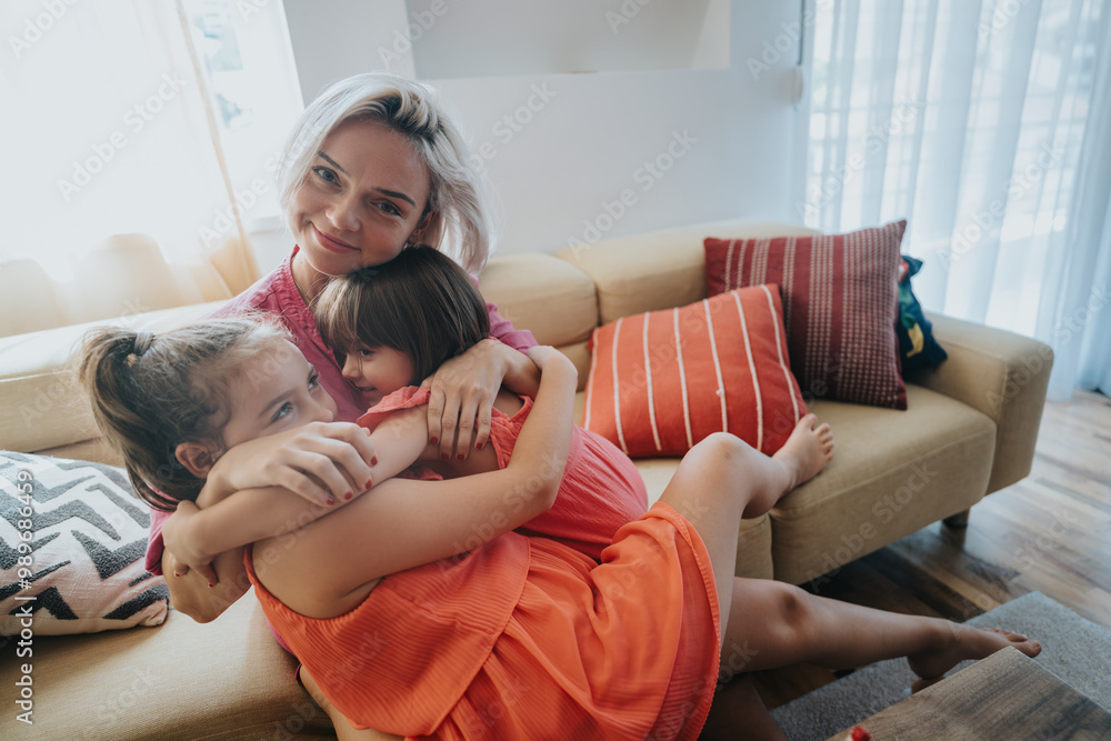 Obraz premium A joyful mother hugs her two young daughters warmly on a comfortable sofa in a bright living room, expressing love and family bonding.