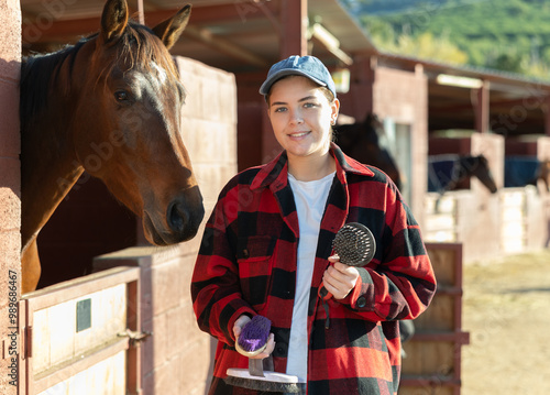 Portrait of young woman with brushes in her hands for cleaning and caring for horses at a horse farm photo