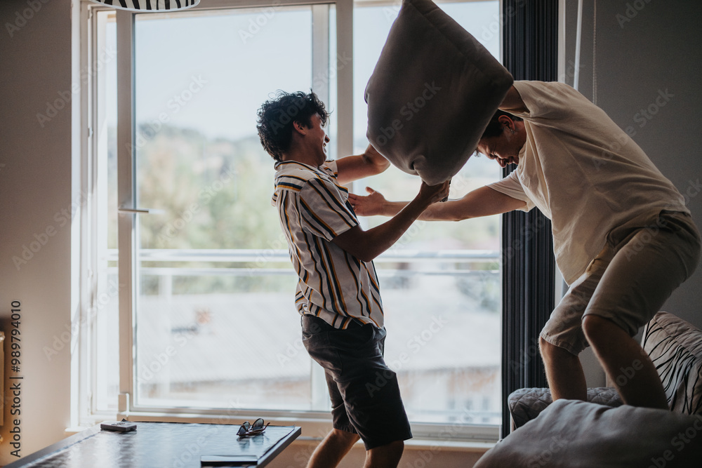 Two friends engage in a fun pillow fight, creating joyful moments and laughter in a bright living room setting. Two friends engage in a fun pillow fight, creating joyful moments and laughter in a bright living room setting.
